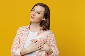 Obraz premium Young kind-hearted sincere thankful woman she 30s wears striped shirt white t-shirt put folded hands on heart look camera isolated on plain yellow background studio portrait. People lifestyle concept.