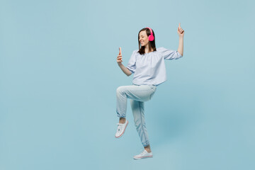 Fototapeta na wymiar Full body young happy fun woman she 20s wears casual blouse headphones listen to music dance raise up hands leg hold mobile cell phone isolated on pastel plain light blue background studio portrait