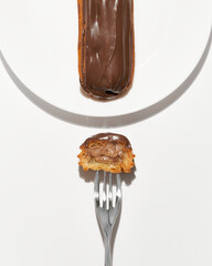 Traditional french eclairs with chocolate with metal kitchen fork isolated on white background. Tasty dessert. Sweet Dessert Pastry filled with cream. Chocolate icing.