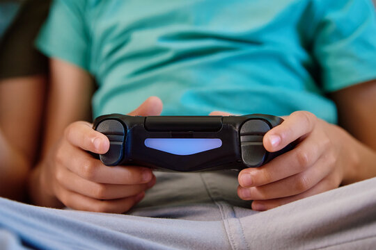 Boy sitting on sofa in living room and playing video game on console with joyctick gamepad in his hand, Online entertainment and leisure activity