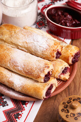 Crunchy rolled pie with ripe cherries on a towel with traditional ornaments. It is served sprinkled with sugar icing.     
