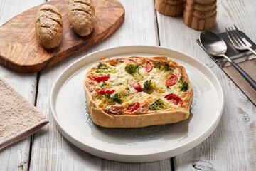 Traditional french pie. Quiche Loraine with broccoli, tomatoes and cheese. Top view, in ceramic baking dish on wooden table. French cuisine.