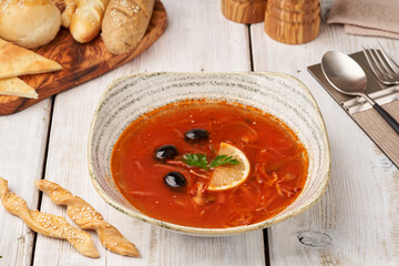 Side view on spicy russian soup solyanka with smoked meats, olives and lemon on the wooden table.   