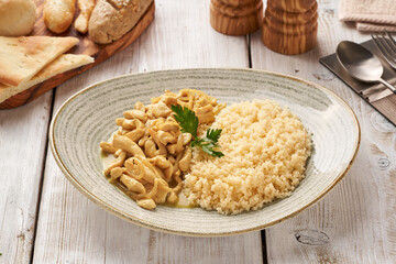 Chicken breast fricassee on a plate with rice. Chicken meat browned and stewed in white wine cream sauce with onion. View from above, close-up.     