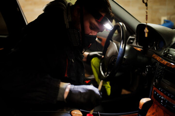 Man in uniform and respirator, worker of car wash center, cleaning car interior cleaning brush . Car detailing concept.