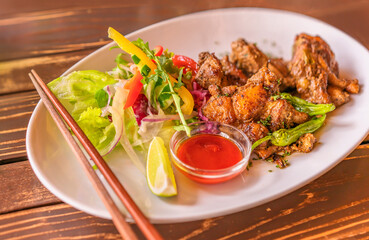 Jamaican jerk chicken plate with vegetables like salada, slices of yellow and red bell peppers, lemon on a plate with chopsticks in a Japanese restaurant of Futamigaura beach of Fukuoka in Kyushu.