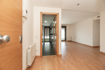 Entrance hall of a house with access to an empty living room with oak flooring and a kitchen with stoneware floors and a wooden and glass door