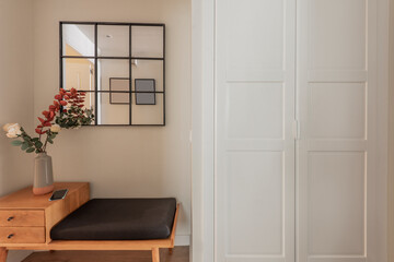 Entrance hall of a house with built-in wardrobe with white wooden doors, cherry wood sideboard with drawers and black framed mirror