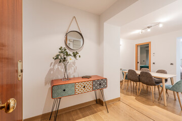 Entrance hall of a house with an orange wooden sideboard with polychrome drawers and access to an...