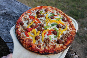 Pizza merguez, poivrons, viande hachée sur planche en bois