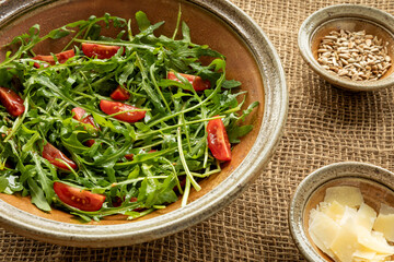 Rocket salad with tomato, cheese flakes and sunflower seeds on jute textile.