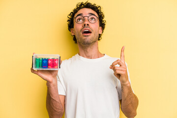 Young caucasian man holding a battery box isolated on yellow background pointing upside with opened mouth.