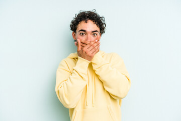 Young caucasian man isolated on blue background covering mouth with hands looking worried.