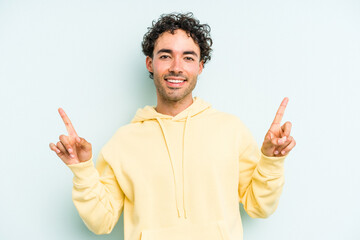Young caucasian man isolated on blue background indicates with both fore fingers up showing a blank...