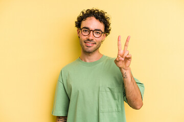 Young caucasian man isolated on yellow background joyful and carefree showing a peace symbol with fingers.