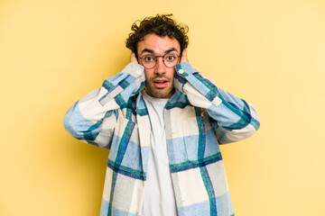 Obraz premium Young caucasian man isolated on yellow background covering ears with hands trying not to hear too loud sound.