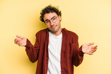 Young caucasian man isolated on yellow background doubting and shrugging shoulders in questioning...