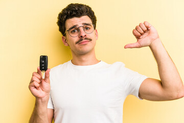 Young caucasian man holding car keys isolated on yellow background feels proud and self confident, example to follow.