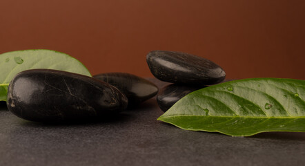 Massage stones with leaves on a dark stone table, spa concept background