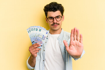 Young caucasian man holding banknotes isolated on yellow background standing with outstretched hand...