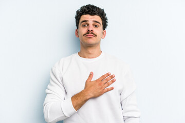 Young caucasian man isolated on blue background taking an oath, putting hand on chest.