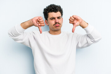 Young caucasian man isolated on blue background showing a dislike gesture, thumbs down....