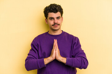 Young caucasian man isolated on yellow background praying, showing devotion, religious person...