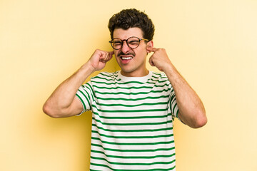 Young caucasian man isolated on yellow background covering ears with fingers, stressed and desperate by a loudly ambient.