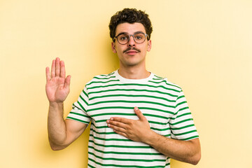 Young caucasian man isolated on yellow background taking an oath, putting hand on chest.