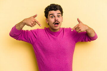 Young caucasian man isolated on yellow background points down with fingers, positive feeling.