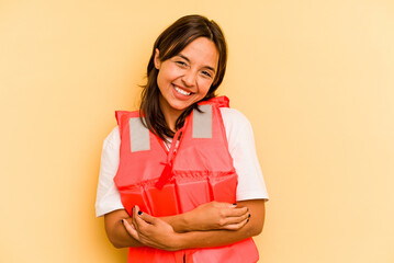 Young hispanic woman holding life jacket isolated on yellow background laughing and having fun.