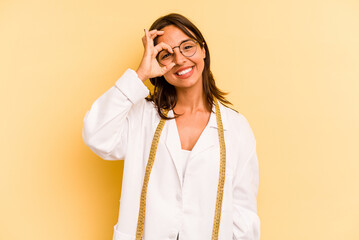 Young nutritionist hispanic woman isolated on yellow background excited keeping ok gesture on eye.