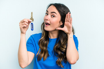 Young caucasian woman holding home keys isolated on blue background trying to listening a gossip.