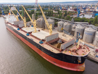 Loading grain into sea cargo vessel in seaport from silos of grain storage. Aerial view