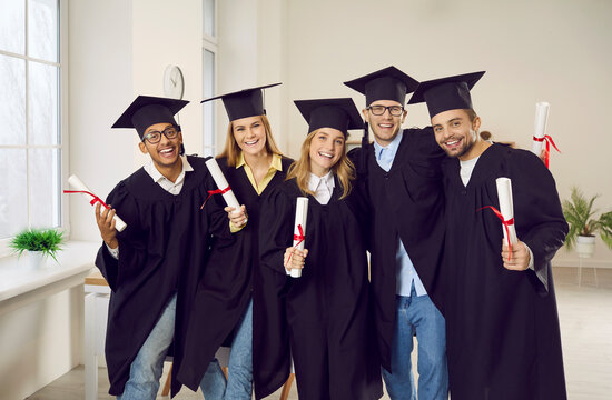 Portrait of smiling diverse students in mantles and hats pose with diplomas celebrate university graduation. Happy college graduates in robes excited with high school finish. Education concept.