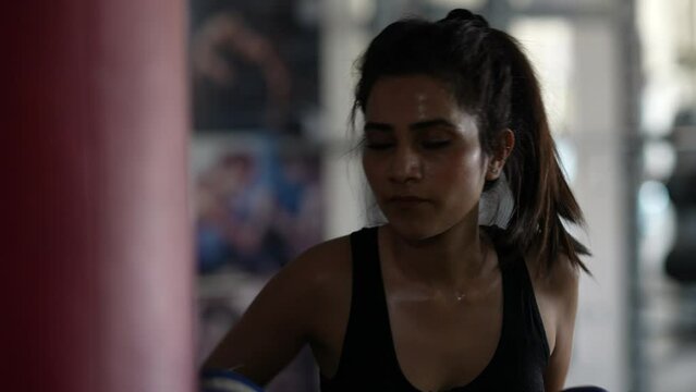 Kickboxing, A young Indian woman fighter trains his punches, beats a punching bag, training day in the boxing gym, strength fit body, Asian girl strikes fast.