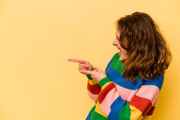 Young caucasian woman isolated on yellow background points with thumb finger away, laughing and carefree.