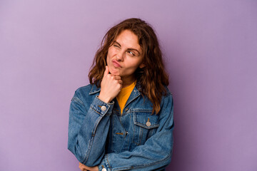 Young caucasian woman isolated on purple background thinking and looking up, being reflective, contemplating, having a fantasy.