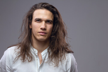 Handsome calm man. Portrait of a young muscular guy with long hair. Strong boy on an isolated grey...