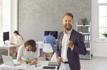 Portrait of handsome young man fist pumping with happy face expression standing against modern...