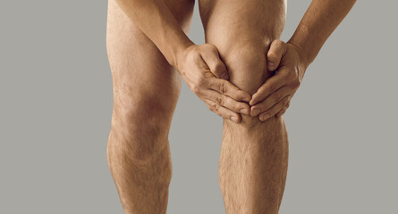 Man suffers from rheumatoid arthritis, feels pain and touches his knee. Fit muscular Caucasian...