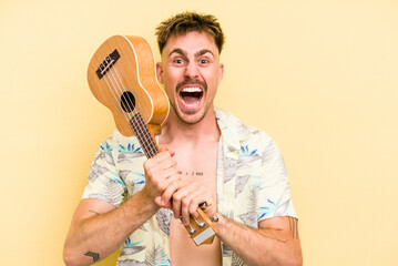 Young caucasian holding a ukulele isolated on yellow background