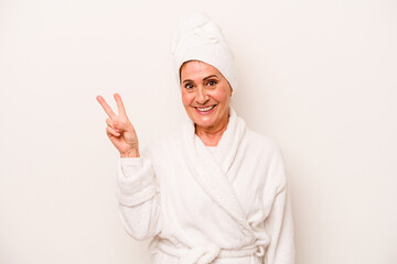 Middle age caucasian woman wearing a bathrobe isolated on white background joyful and carefree showing a peace symbol with fingers.