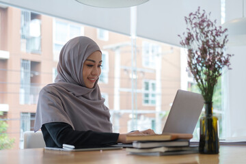 Obraz na płótnie Canvas Young female entrepreneur wearing a hijab sitting at modern office and using laptop computer.