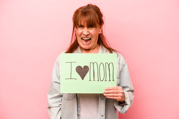 Fototapeta na wymiar Middle age caucasian woman holding I love mom placard isolated on pink background screaming very angry and aggressive.