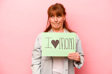 Middle age caucasian woman holding I love mom placard isolated on pink background confused, feels doubtful and unsure.