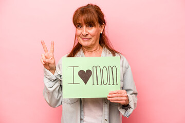 Fototapeta na wymiar Middle age caucasian woman holding I love mom placard isolated on pink background showing number two with fingers.