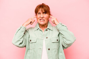 Middle age caucasian woman isolated on pink background covering ears with fingers, stressed and desperate by a loudly ambient.
