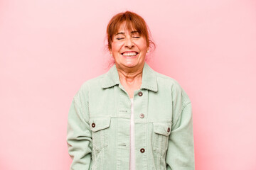 Middle age caucasian woman isolated on pink background laughs and closes eyes, feels relaxed and happy.