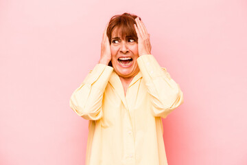 Middle age caucasian woman isolated on pink background covering ears with hands trying not to hear too loud sound.